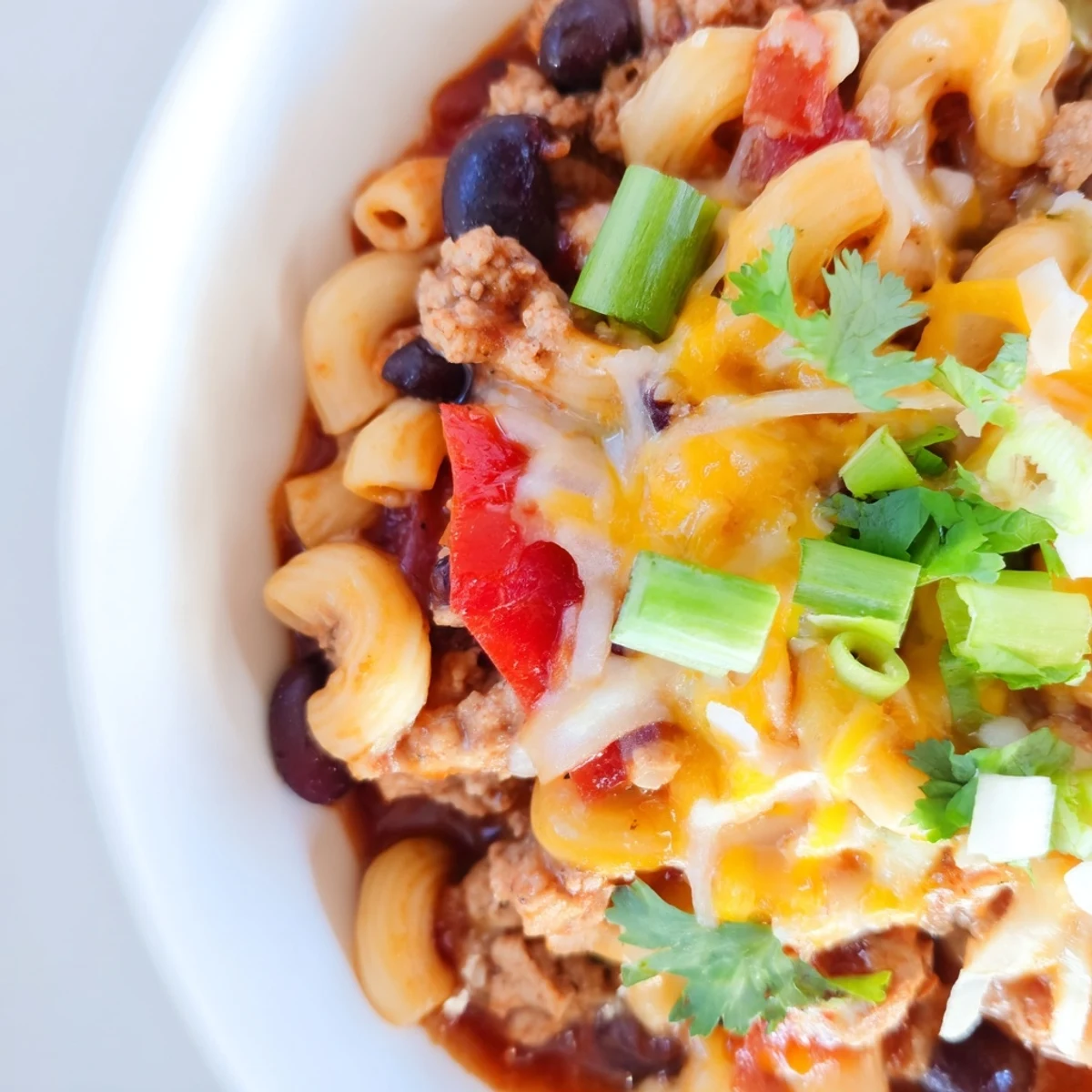 A white bowl filled with Turkey Chili Mac and Cheese with Cheddar is served next to a slice of crusty bread.