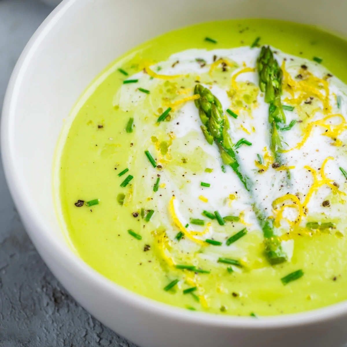 Creamy Asparagus Soup with Lemon served hot in a white bowl, garnished with fresh chives and reserved asparagus tips.