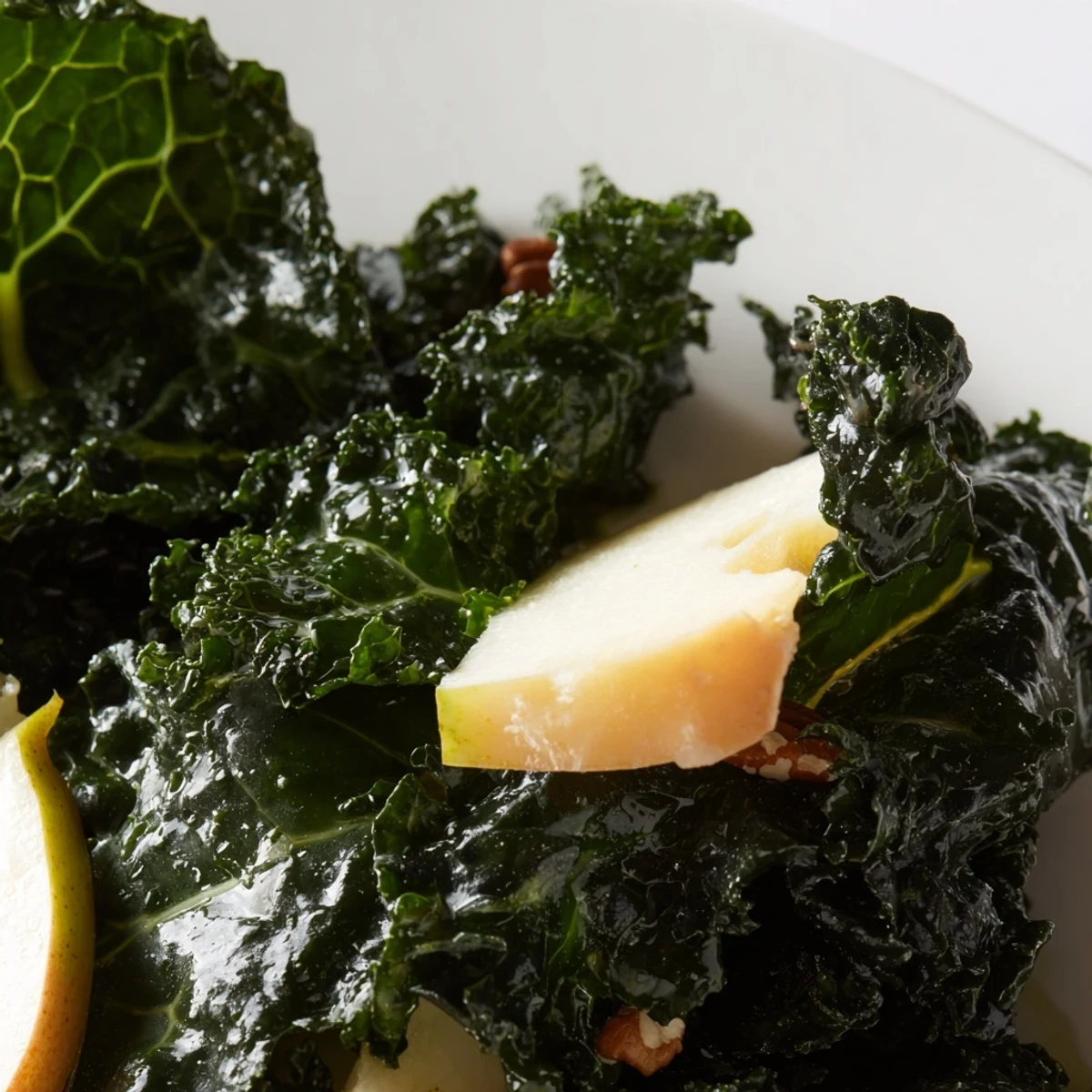 A bowl of Winter Kale Salad with Apple and Sharp Cheddar with chopped pecans and red onion.