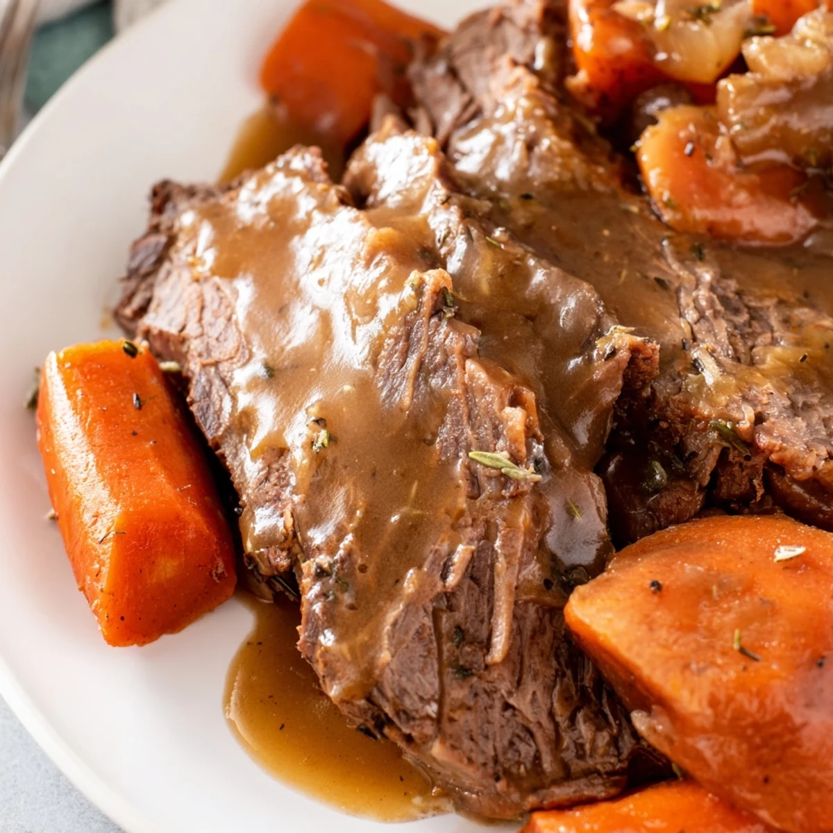 Carved slices of Slow Cooker Roast Beef with Gravy showcase the tender, shredded texture, accompanied by roasted vegetables and a generous drizzle of homemade gravy.