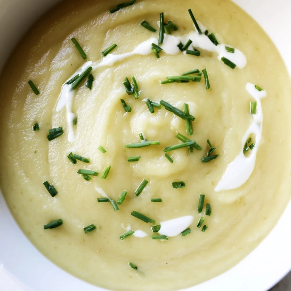 Spoon dipping into creamy leek and potato soup, served hot with crusty bread alongside.