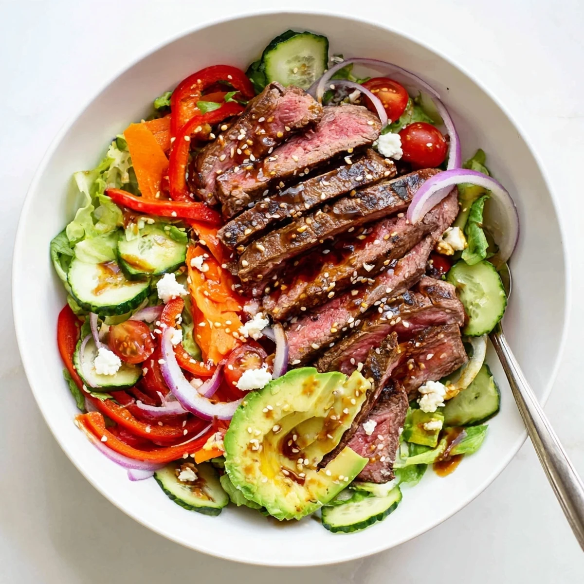 A close-up of a vibrant Beef Salad Bowl with Dressing, showing tender grilled beef slices, crisp cucumber, and creamy avocado atop fresh greens.  
