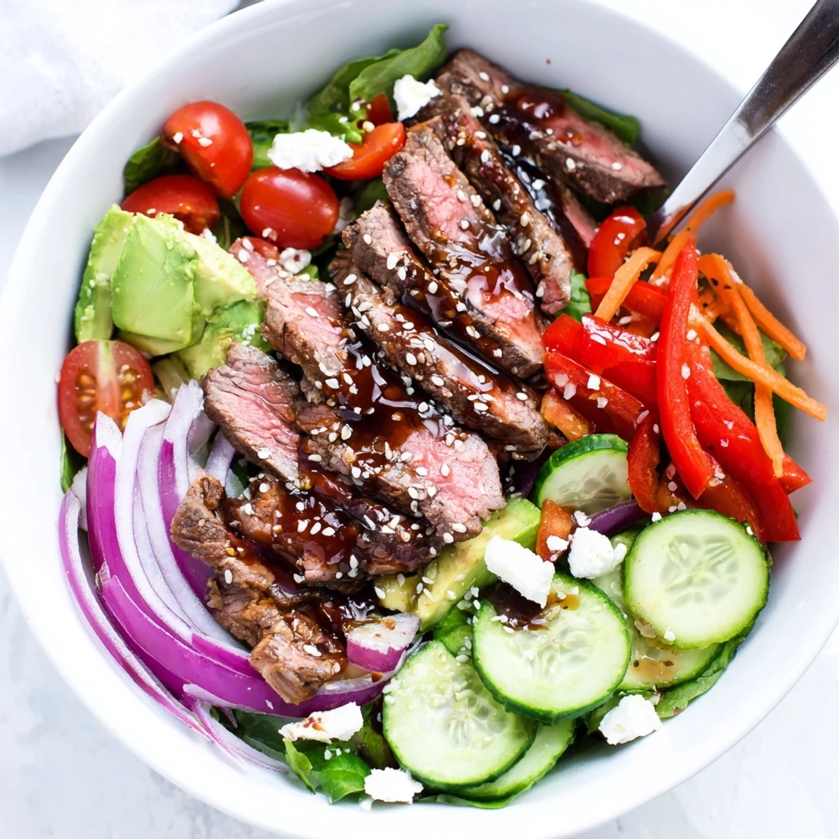 An overhead view of a Beef Salad Bowl with Dressing, highlighting juicy cherry tomatoes, julienned carrots, and sesame seeds, ready to serve.