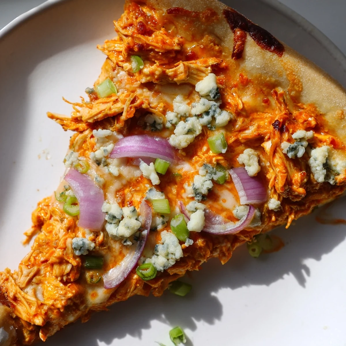 Oven-baked MVP Buffalo Chicken Pizza topped with shredded buffalo chicken, blue cheese crumbles, and red onion slices.