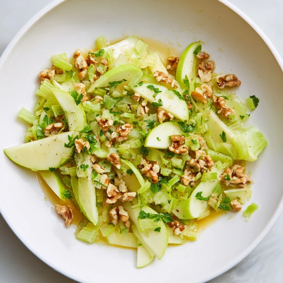 Freshly sliced green apples and celery combined with toasted walnuts for a crisp Green Apple and Celery Salad with Walnuts, garnished with parsley. 