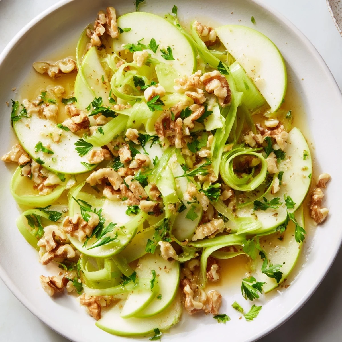 A large bowl of vibrant Green Apple and Celery Salad with Walnuts tossed in a light dressing, ready to be served as a refreshing side. 