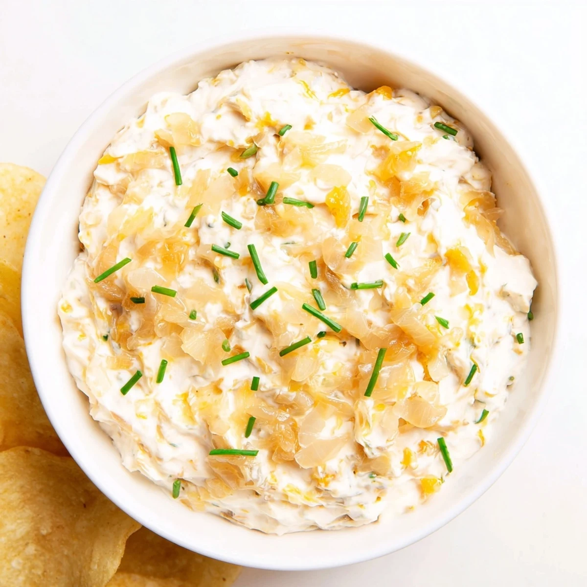 A close-up of golden caramelized onions folded into creamy Game Day Onion Dip, served with crispy ruffled potato chips on a wooden platter.
