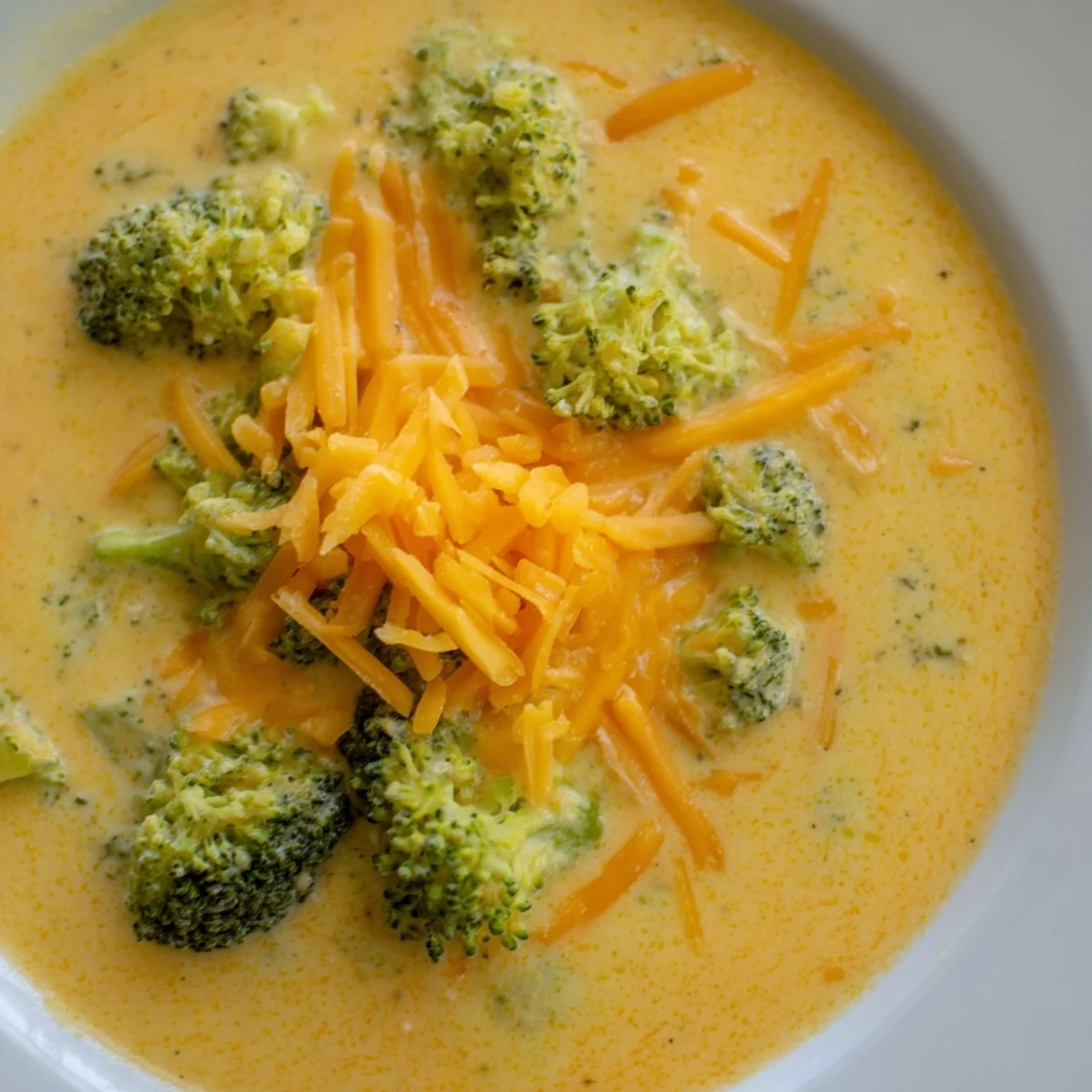 Velvety Creamy Broccoli Cheddar Soup with tender broccoli florets and melted sharp cheddar in a rustic ceramic bowl.  