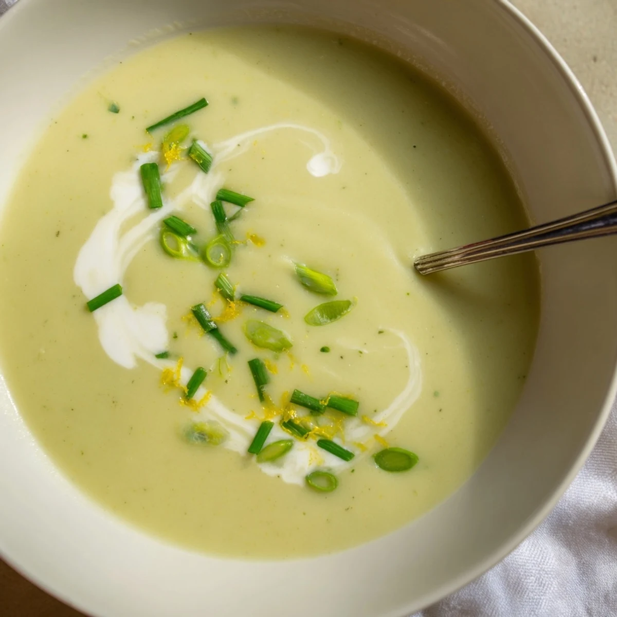 Creamy Asparagus Soup with Lemon in a white bowl, garnished with fresh dill and lemon zest, steam rising. 