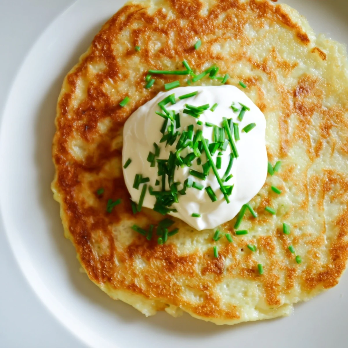 Golden-brown Irish Boxty with Sour Cream displayed on a white plate, garnished with fresh chives for a traditional appetizer.