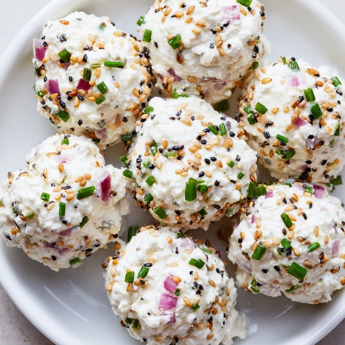 A serving plate of Everything Bagel Cottage Cheese Bites paired with sliced cucumbers and red bell peppers offers a fresh, crunchy contrast.