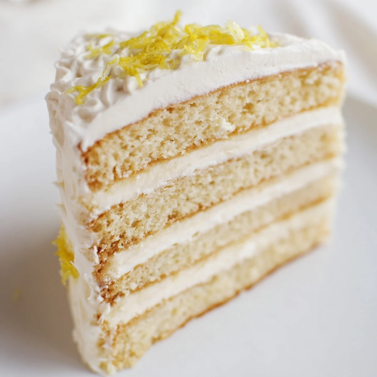 Golden layers of Limoncello Mascarpone Cake on a white plate, with limoncello syrup brushed on sponge and creamy frosting swirled around the sides.