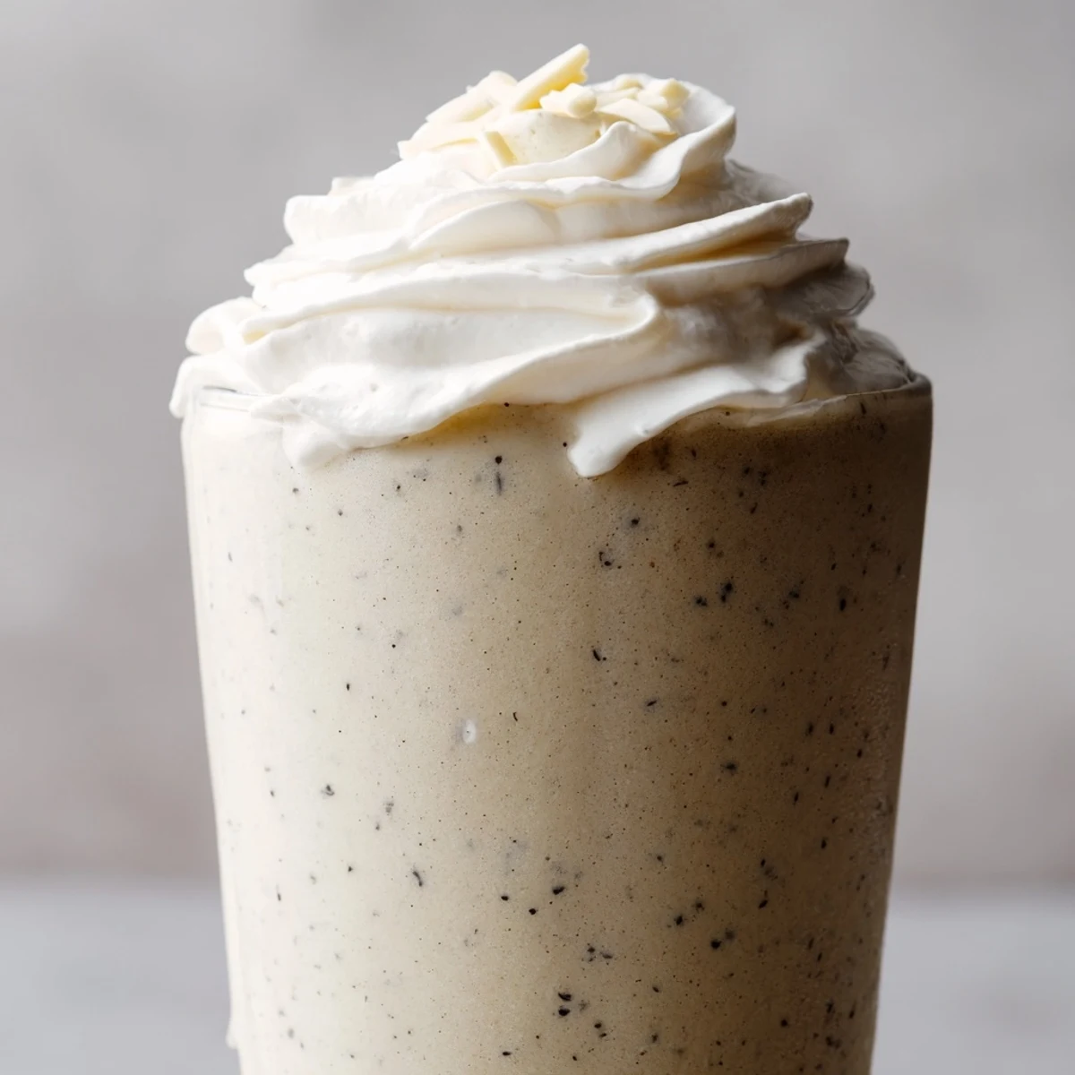 A frosty Vanilla Bean Frappuccino topped with whipped cream and white chocolate shavings in a tall glass.