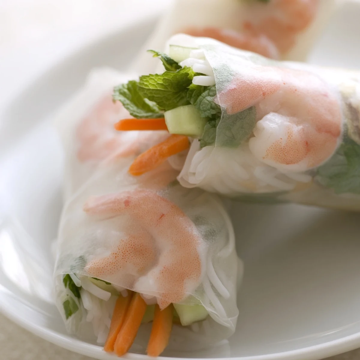 Freshly rolled Vietnamese Spring Rolls with vibrant carrots and herbs on a plate.
