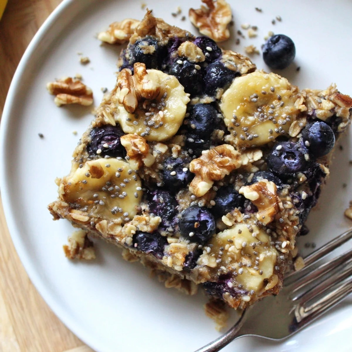 A warm slice of the High Protein Banana Blueberry Breakfast Bake with visible oats and juicy berries.