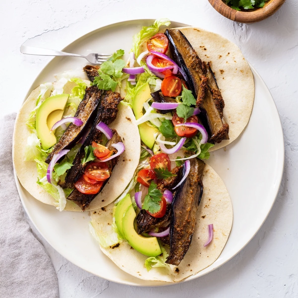 Charred eggplant tacos displayed on a plate with lime wedges and cilantro garnish.