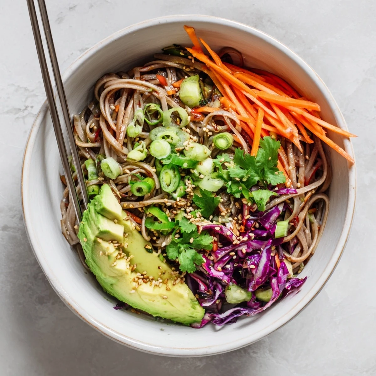 Vibrant bowl of sesame avocado and soba noodle salad with julienned carrots and red cabbage, perfect for a light lunch.