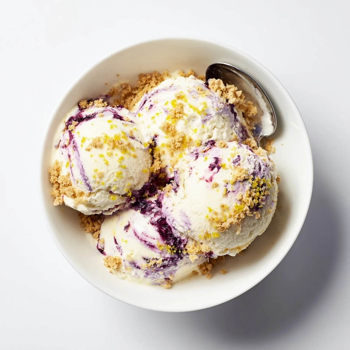 Creamy Lemon Blueberry Cheesecake Ice Cream scoops into a bowl with graham cracker crumbs and fresh blueberry swirls.