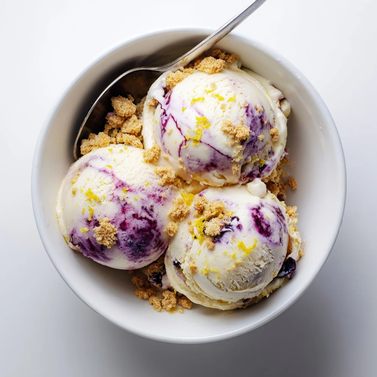 Lemon Blueberry Cheesecake Ice Cream in a waffle cone, drizzled with blueberry sauce and topped with a lemon slice.