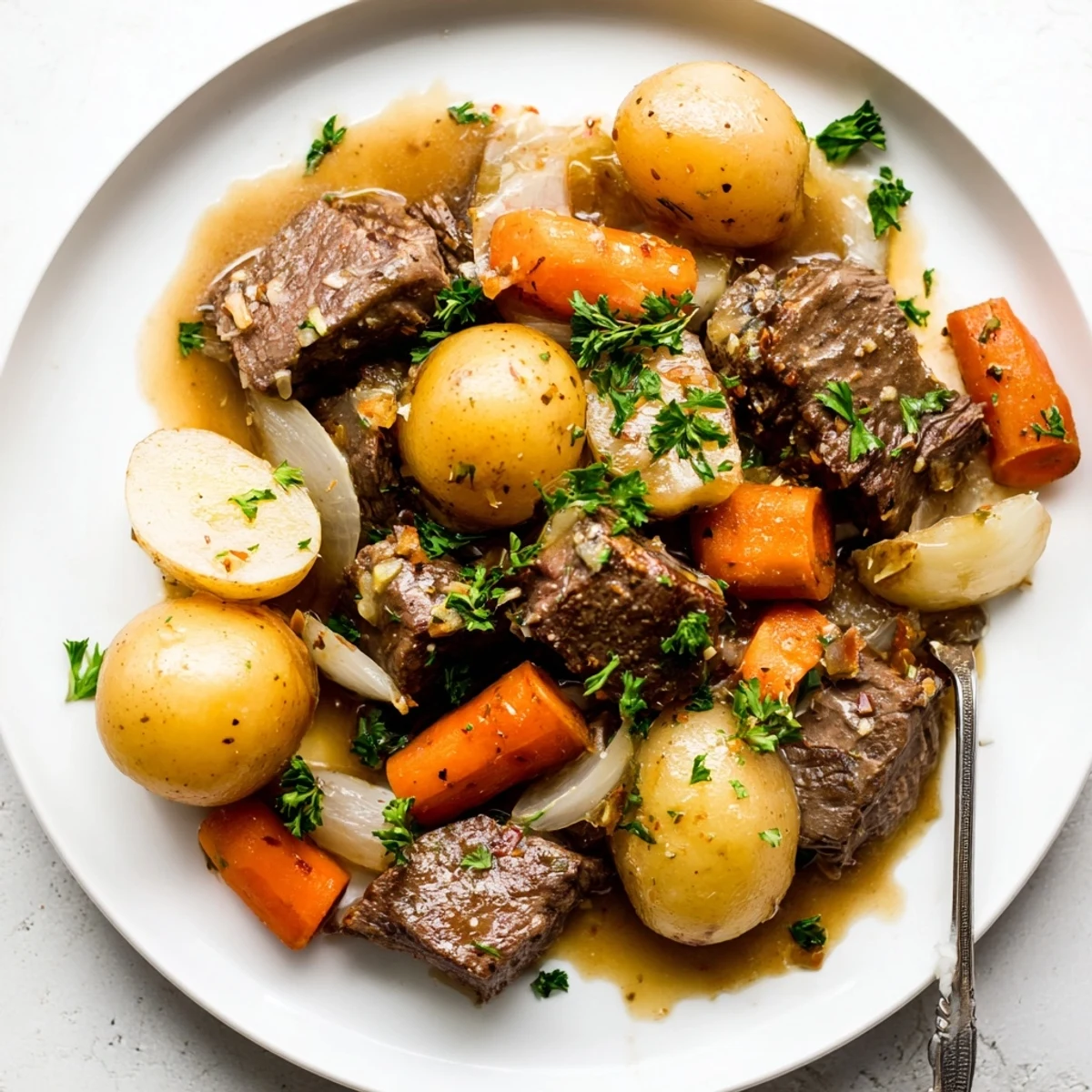 A close-up of tender beef cubes and halved baby potatoes coated in a glossy garlic butter sauce, garnished with fresh parsley.