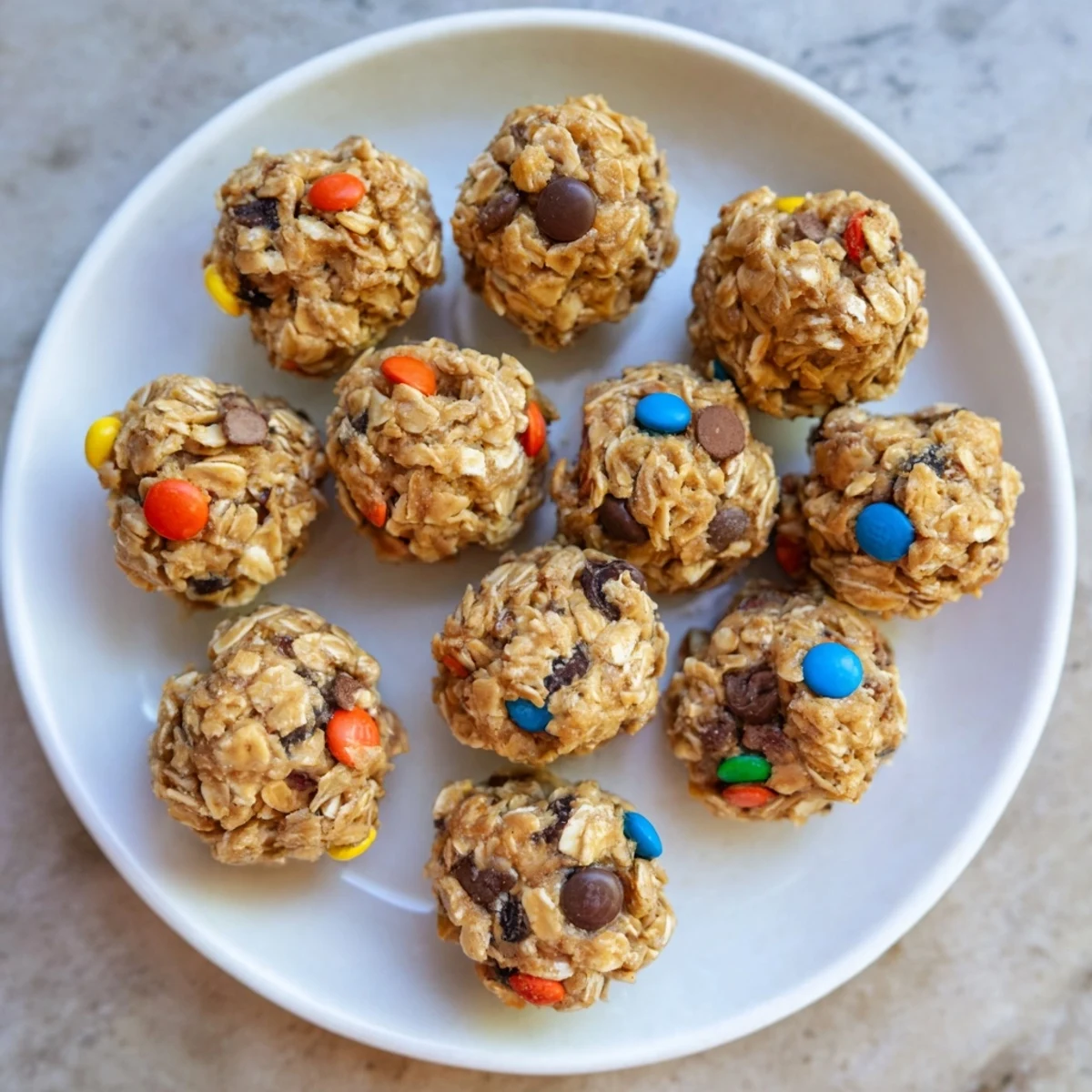 A close-up of homemade Monster Cookie Protein Balls on a rustic wooden board, showing rolled oats and candy-coated chocolates in a chewy texture.
