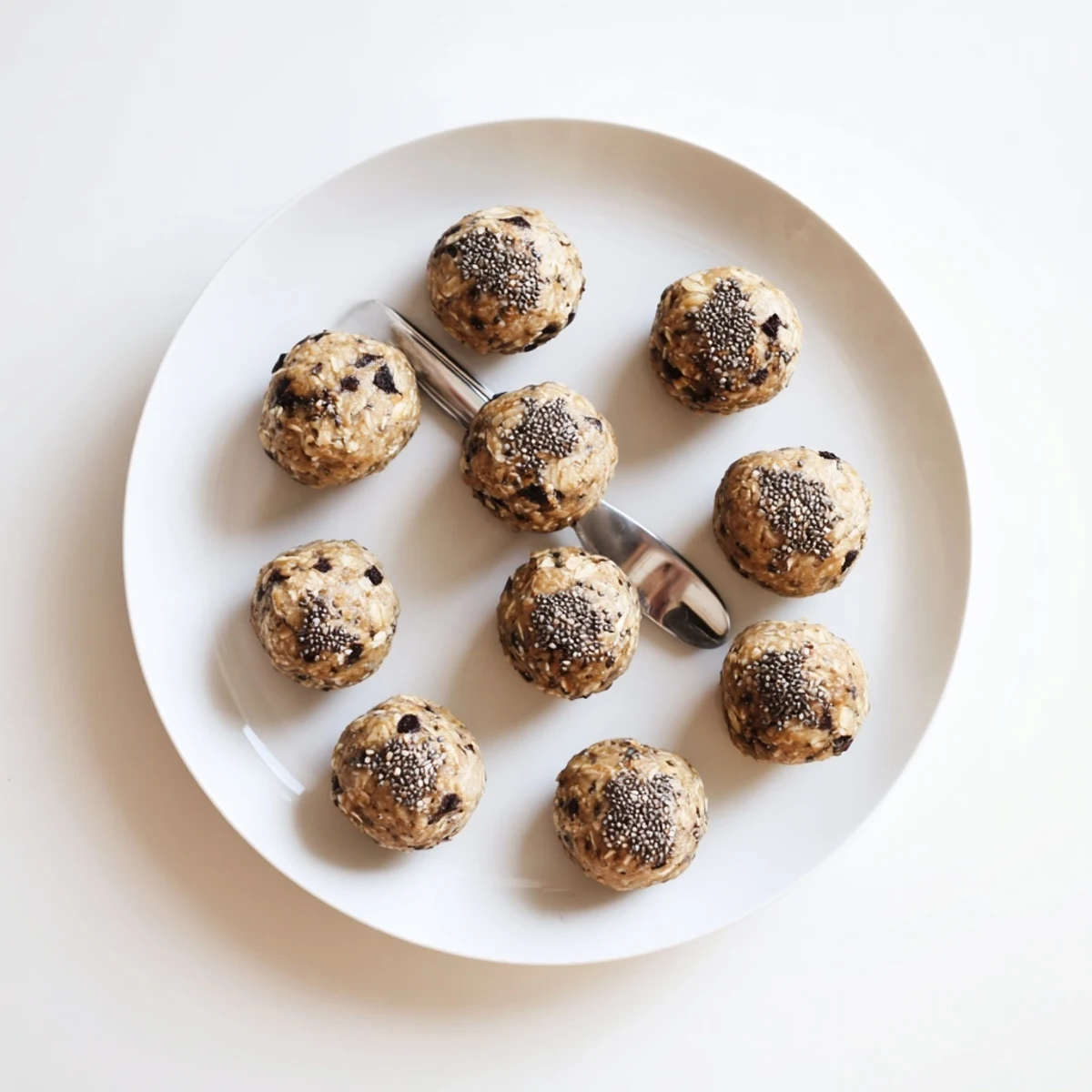 Fresh mint chocolate chip protein balls in a clear glass bowl with a scoop of protein powder beside them.