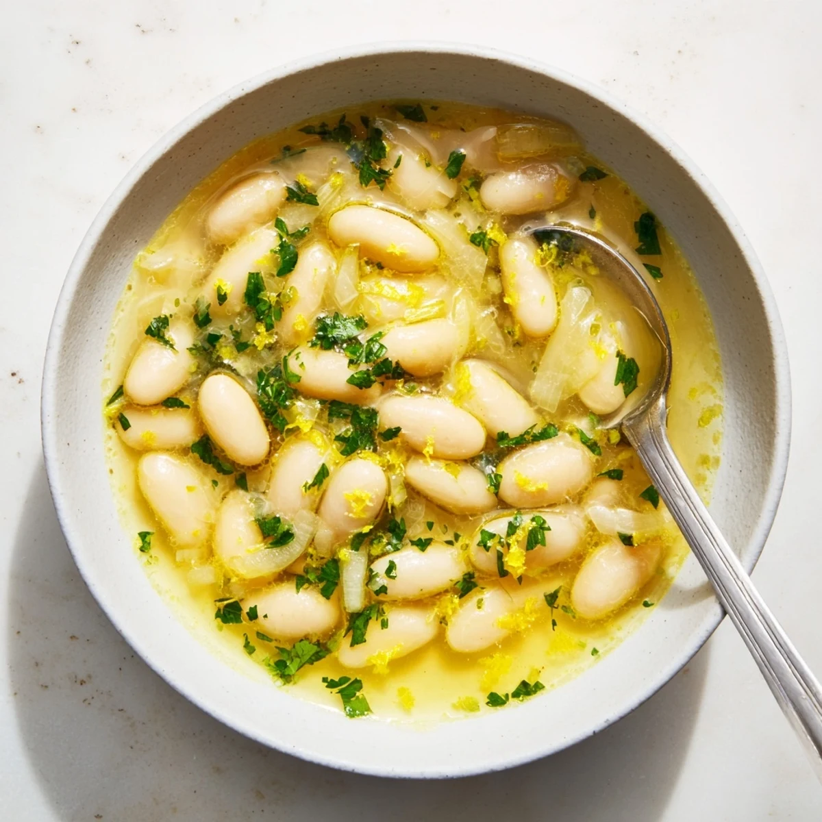 A warm bowl of Miso Butter Brothy Beans garnished with fresh parsley and lemon zest.