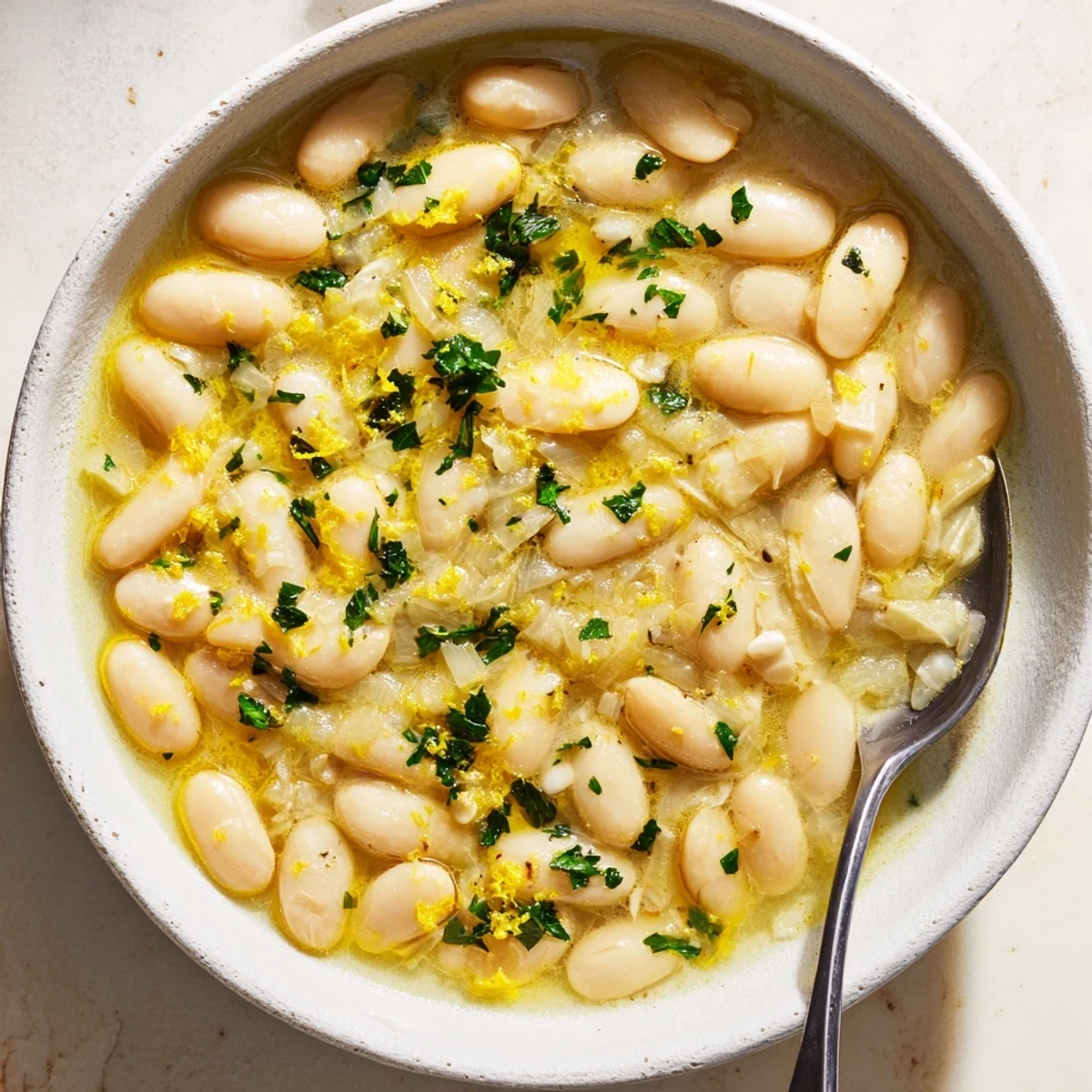 Rich Miso Butter Brothy Beans served hot in a rustic bowl with herbs and a spoon.