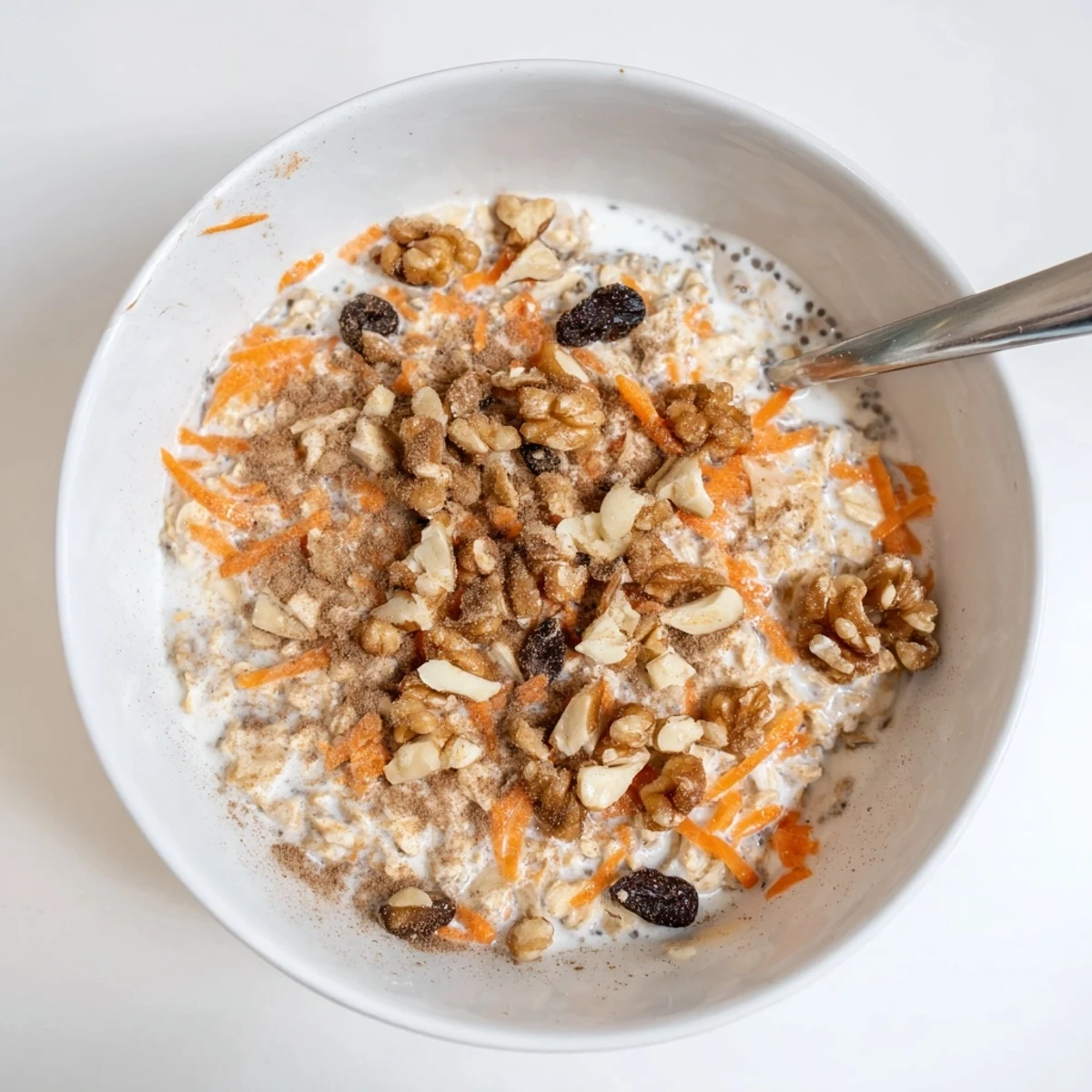 Creamy carrot cake overnight oats topped with chopped walnuts, raisins, and coconut flakes in a glass jar