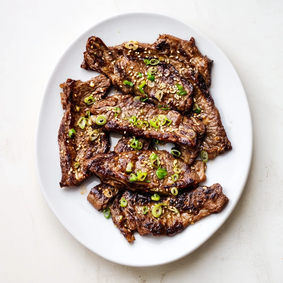 Caramelized Korean Galbi grilled ribs with charred edges and sesame garnish on a white platter