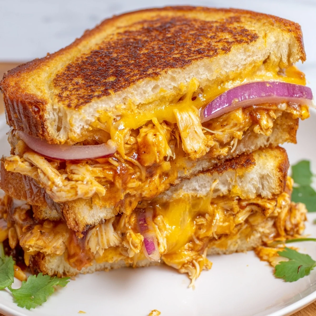 Plate of BBQ chicken grilled cheese featuring a diagonal cut revealing the cheesy BBQ chicken filling inside the crispy crust