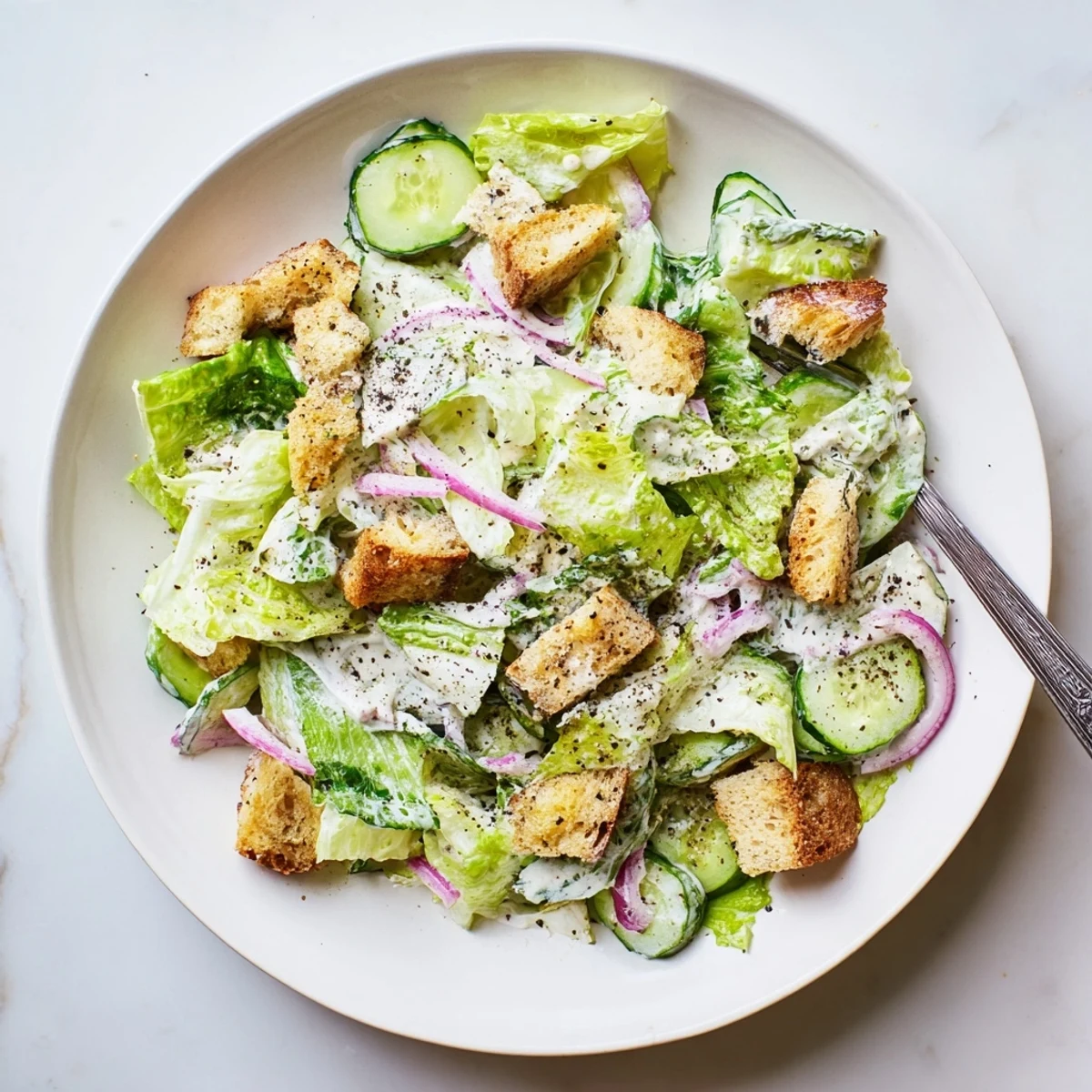 Fresh cucumber Caesar salad with crisp romaine, golden croutons, and creamy Parmesan dressing in a white bowl