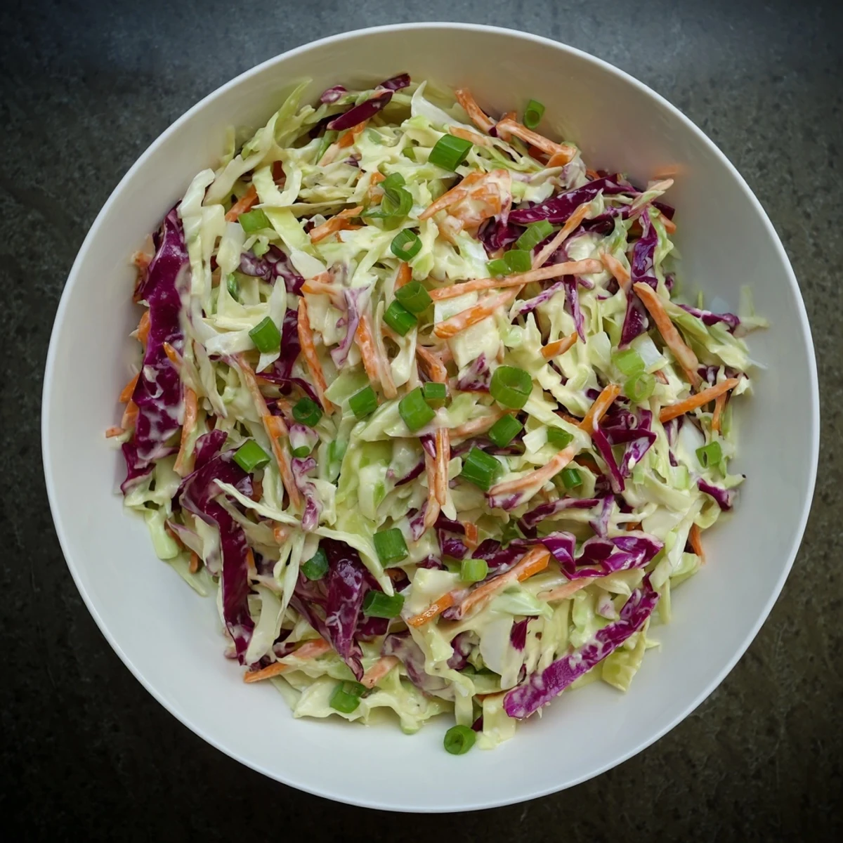 Easy creamy coleslaw served in a white bowl atop a rustic wooden table with napkin.