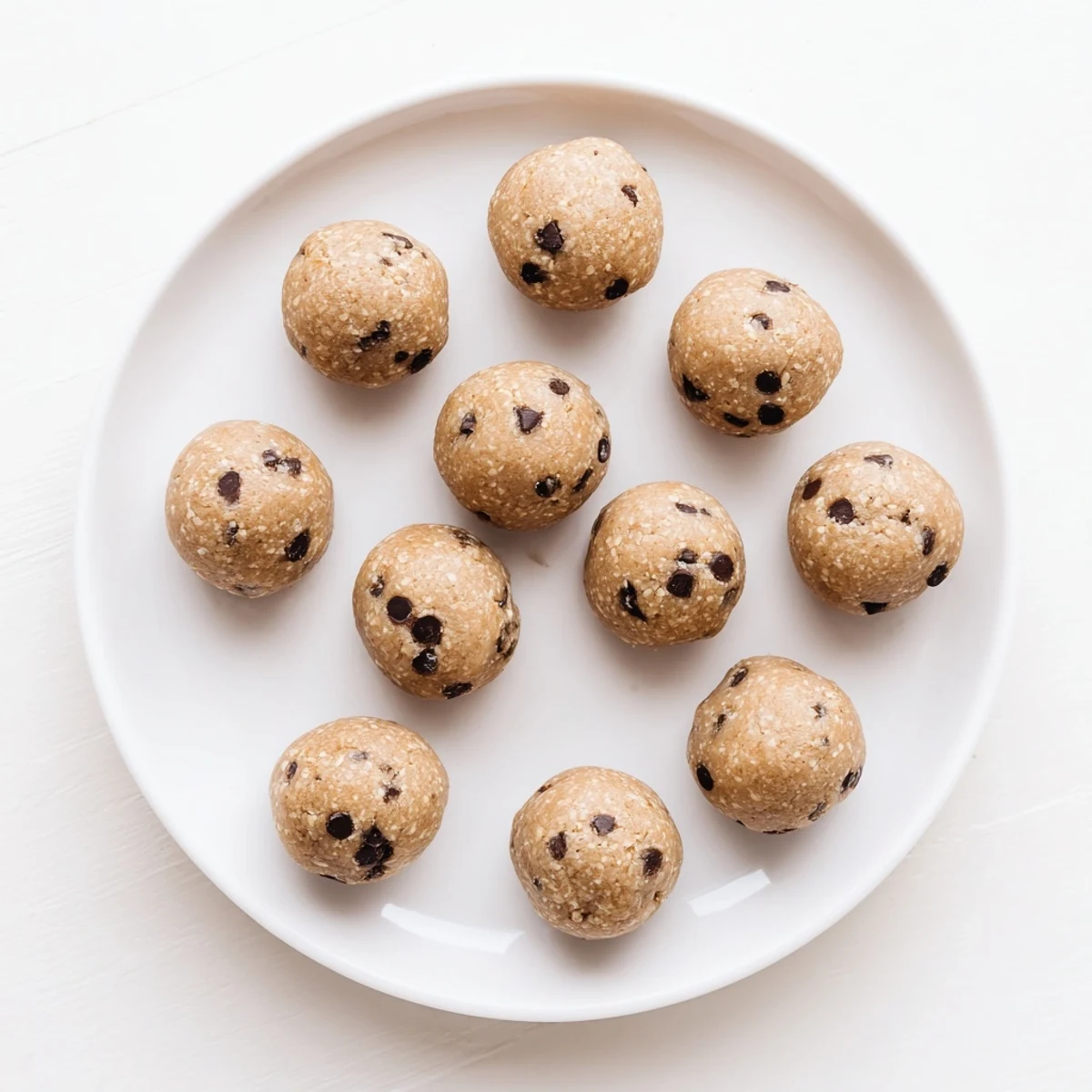 No-bake chocolate chip cookie dough protein balls stacked on a wooden cutting board with oaty texture