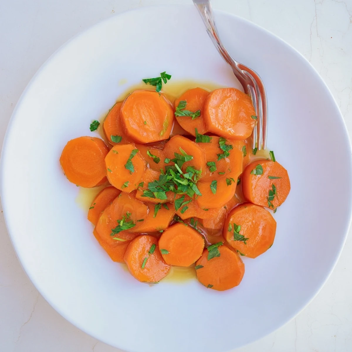 Golden glazed carrots glistening with buttery brown sugar coating on a white serving plate