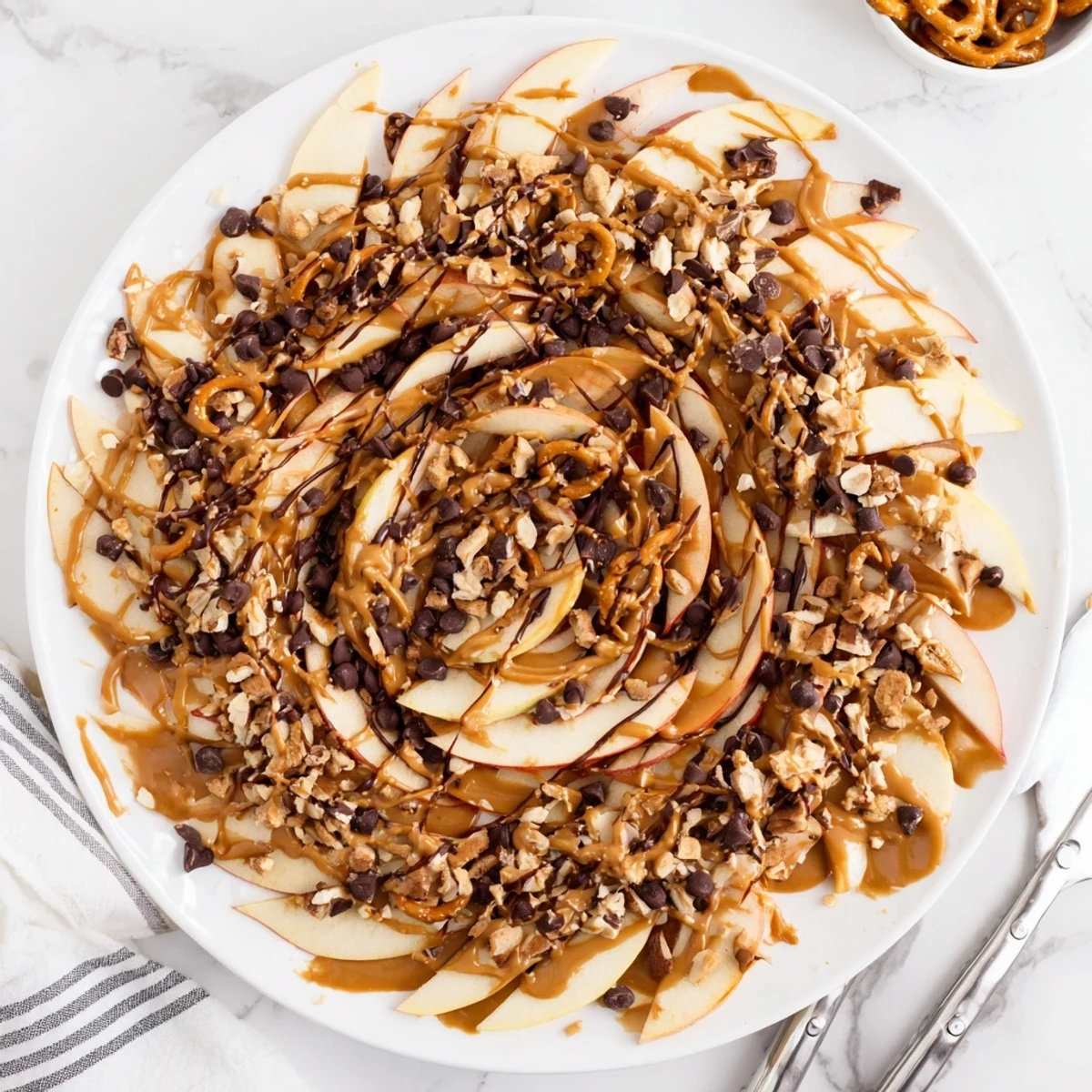 Fresh apple nachos with peanut butter and chocolate drizzle topped with crunchy peanuts and pretzels