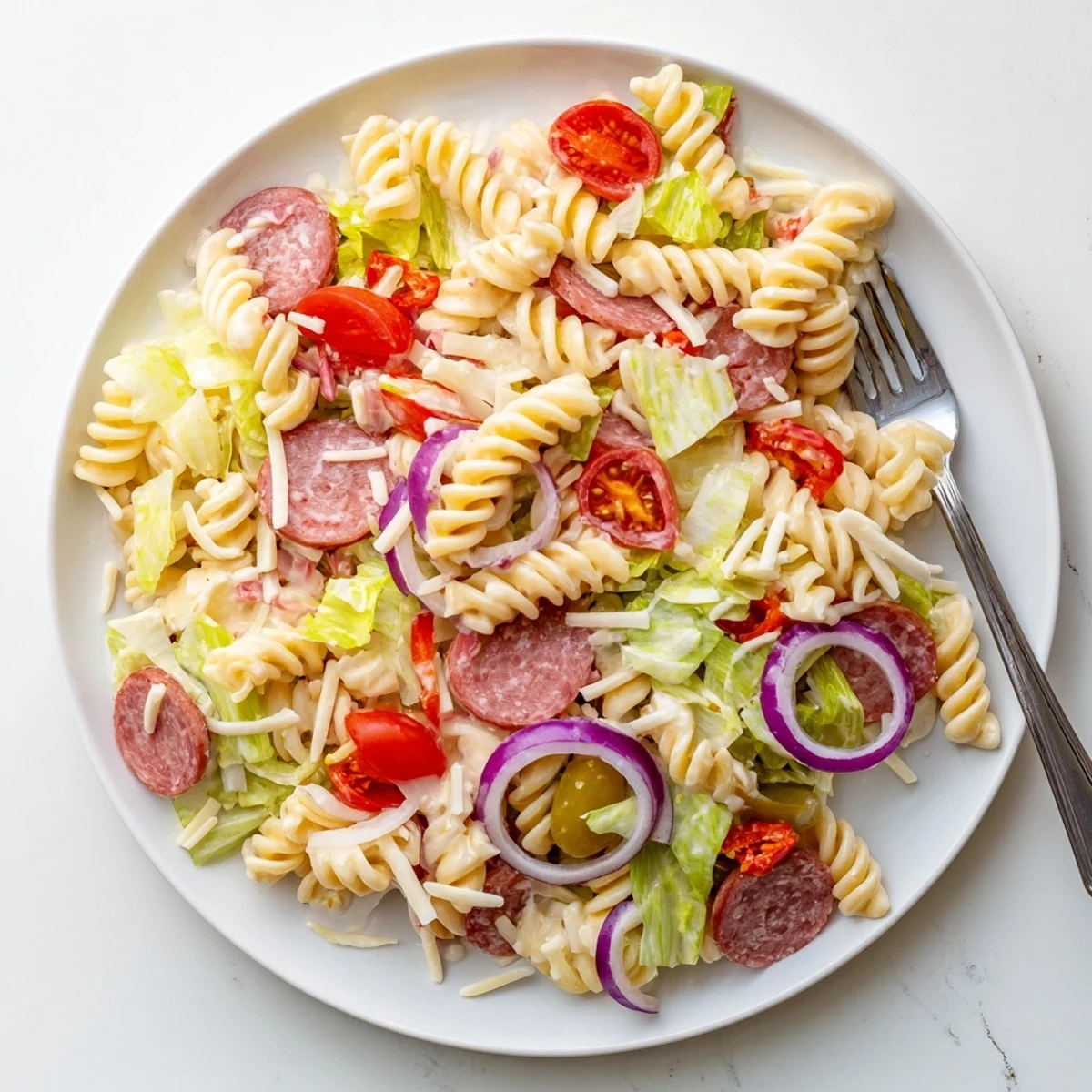 Colorful grinder pasta salad mounded in a serving bowl with cherry tomatoes, provolone, and salami.