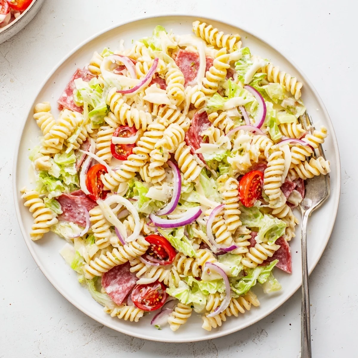Vibrant cold grinder pasta salad featuring rotini noodles, ham, peppers, and cheese in a white bowl.