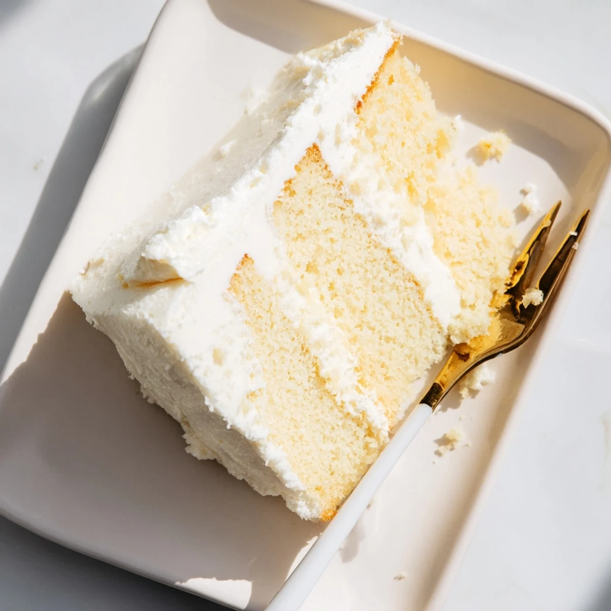Golden church cake square topped with creamy vanilla frosting on a white plate