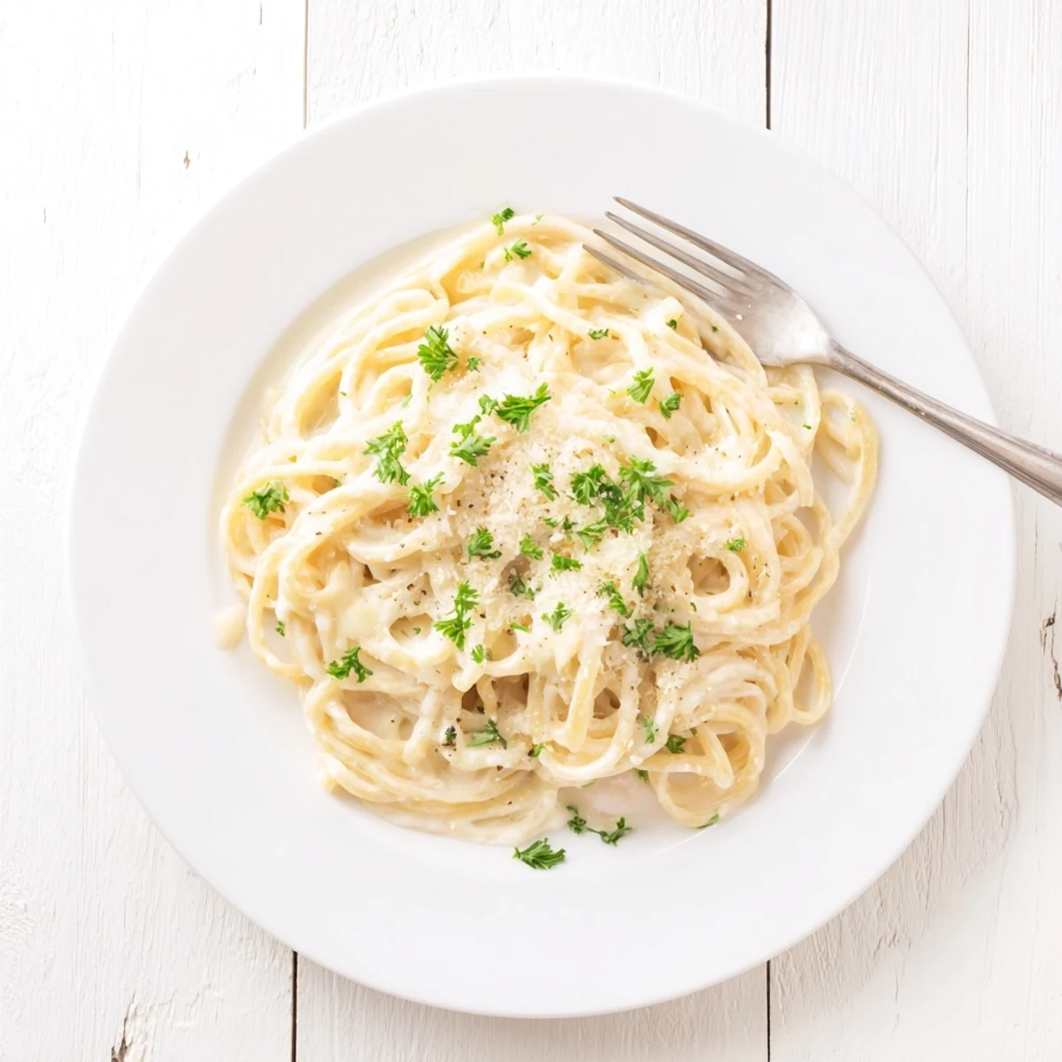Steaming plate of garlic Parmesan spaghetti coated in melted cheese sauce with black pepper specks visible