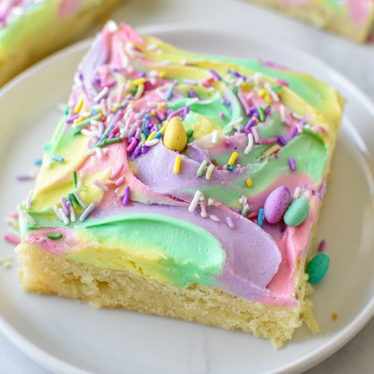 Thick-cut Easter sugar cookie bars topped with creamy pink buttercream and colorful festive sprinkles