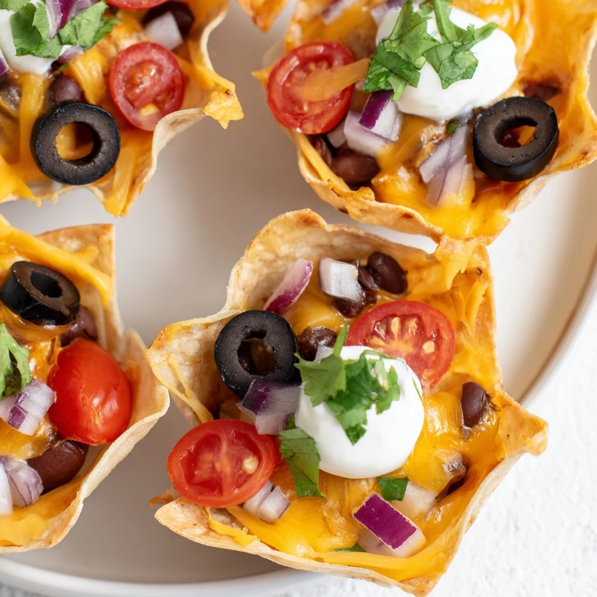 Golden cheesy nacho cups bubbling with melted cheddar and colorful fresh toppings in muffin tin