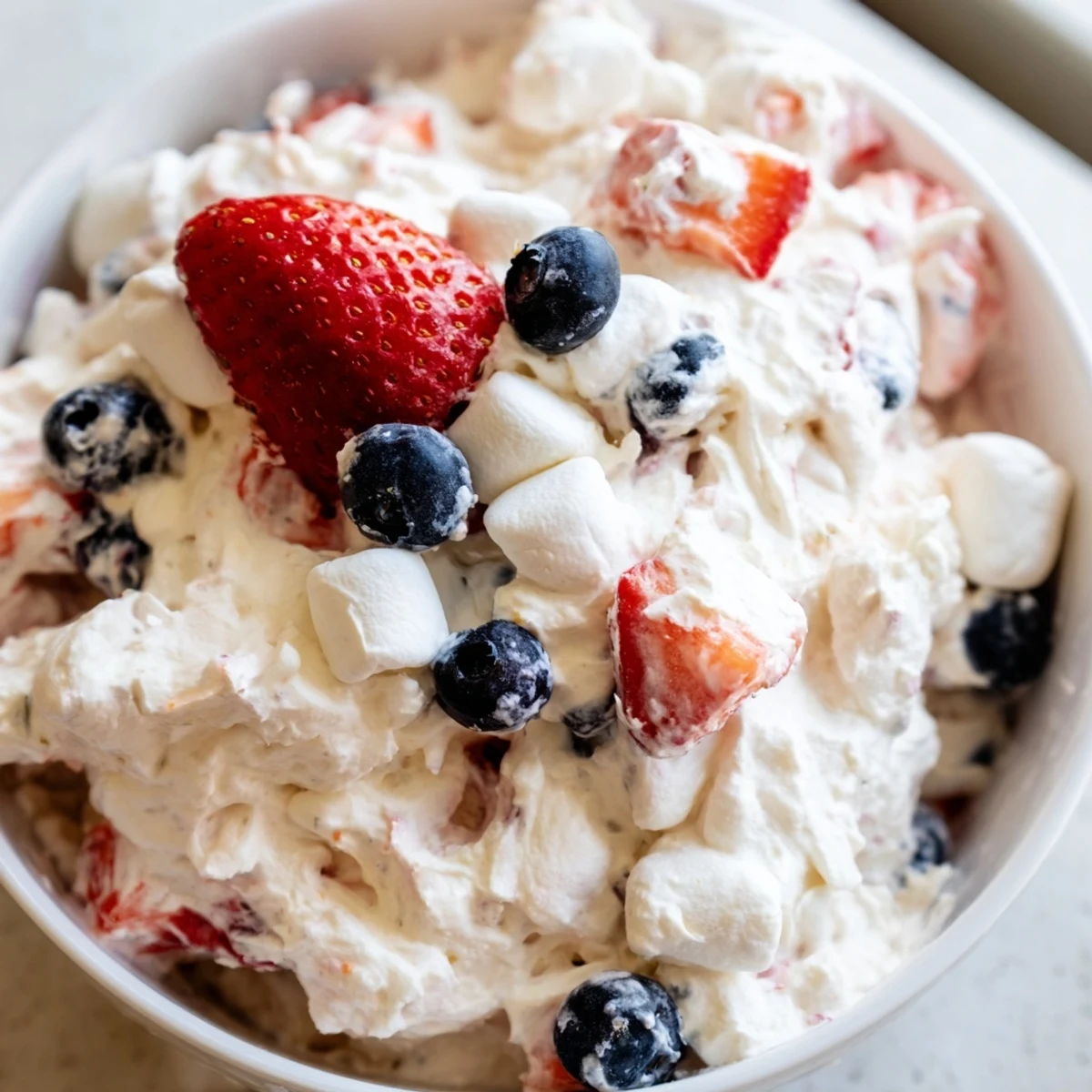 Creamy red white blue cheesecake salad topped with fresh strawberries and blueberries in a glass bowl