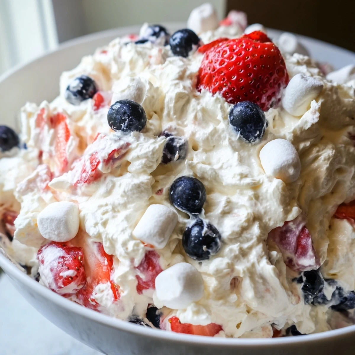 Vibrant red white blue cheesecake salad scooped into individual dessert cups garnished with ripe sweet berries