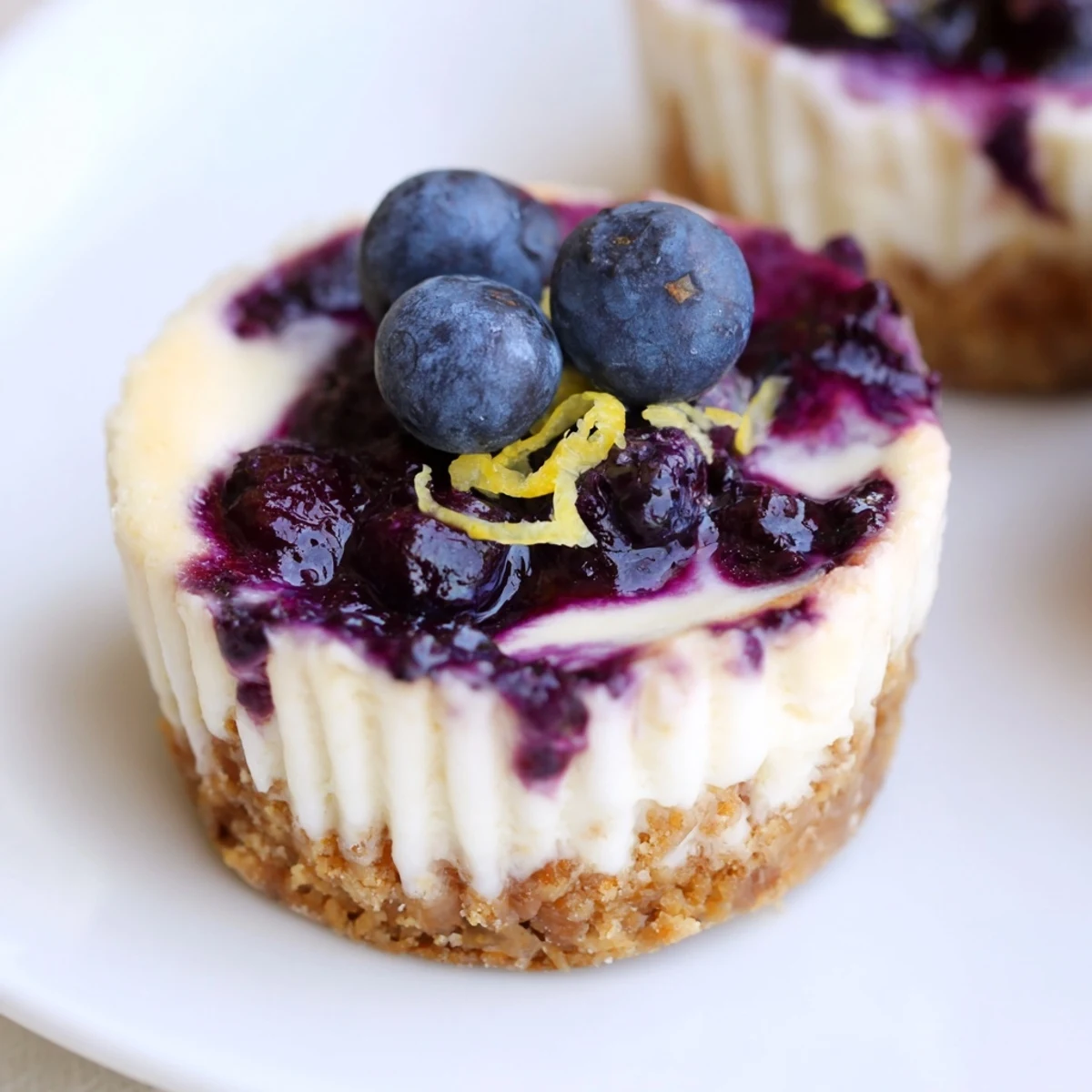 Creamy mini lemon blueberry cheesecakes with graham crusts swirled with vibrant purple berry sauce