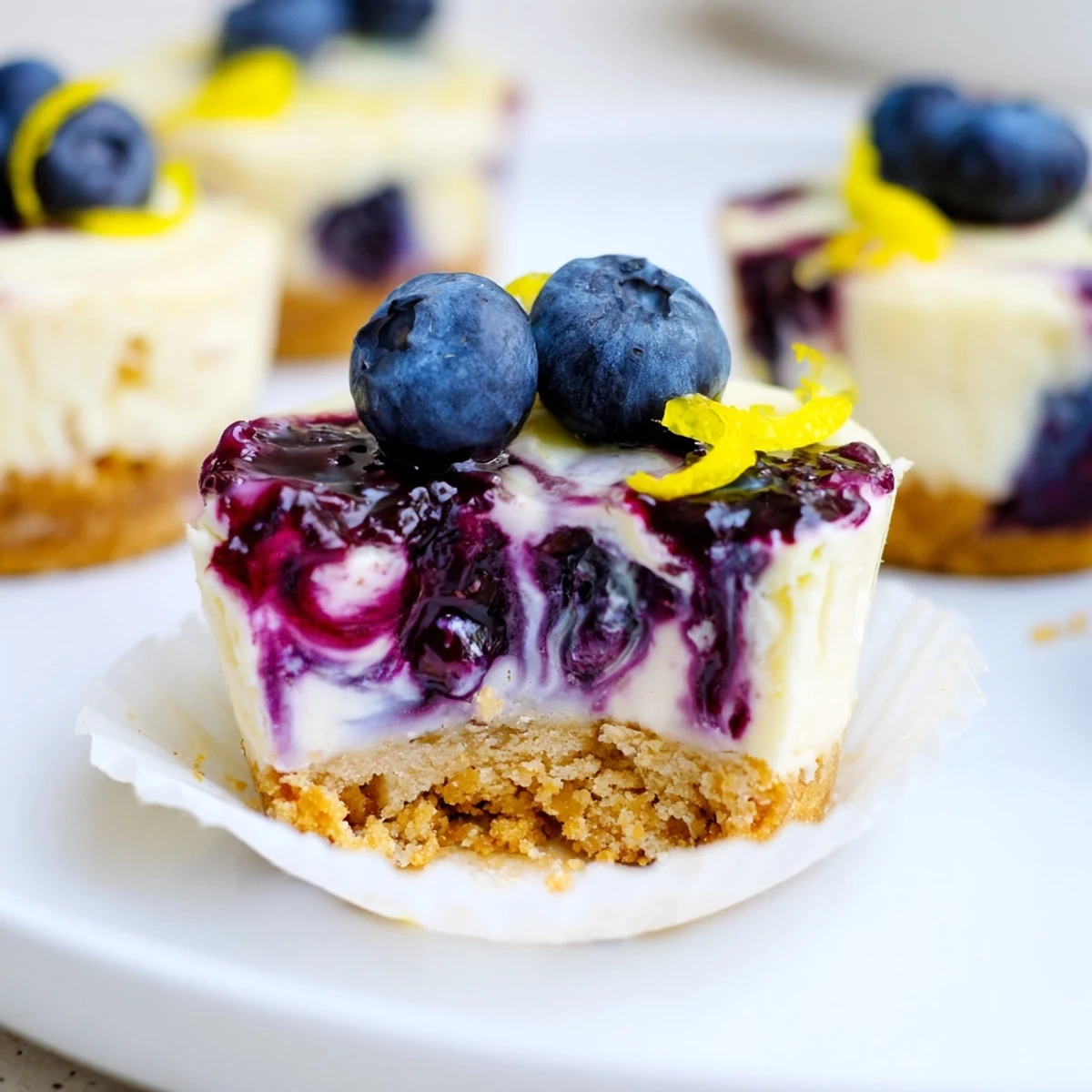 Mini lemon blueberry cheesecakes topped with glossy jewel-toned compote on a rustic white plate