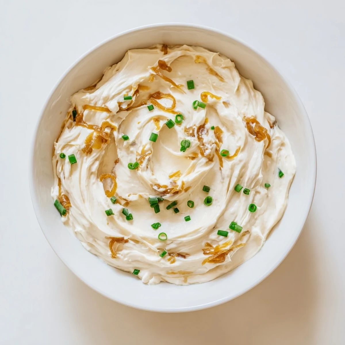 Bowl of homemade French onion dip garnished with green onions alongside vegetable crudités for dipping