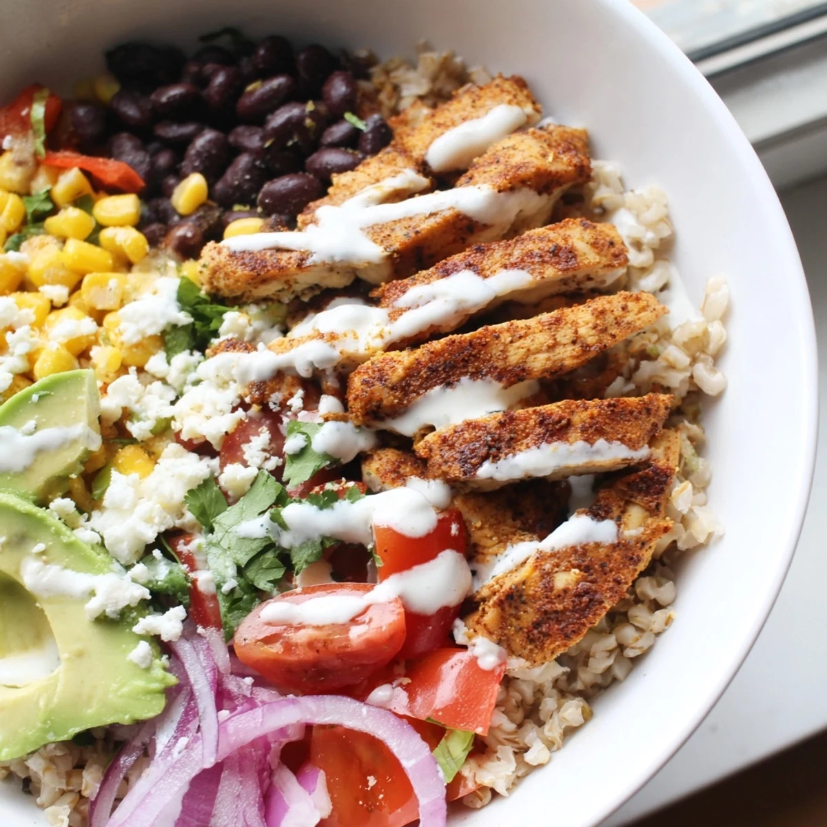 Hearty Mexican chicken grain bowl garnished with cilantro, ripe avocado slices, and a bright lime wedge