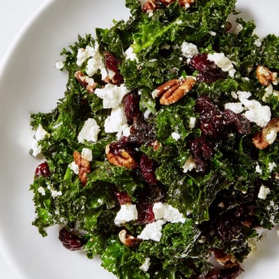 A close-up of the Winter Kale Salad shows ruby cranberries and tangy maple vinaigrette coating the leaves.